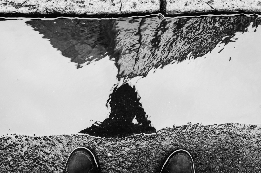 A imagem é uma fotografia do reflexo de Diego Quadros numa poça d'água.